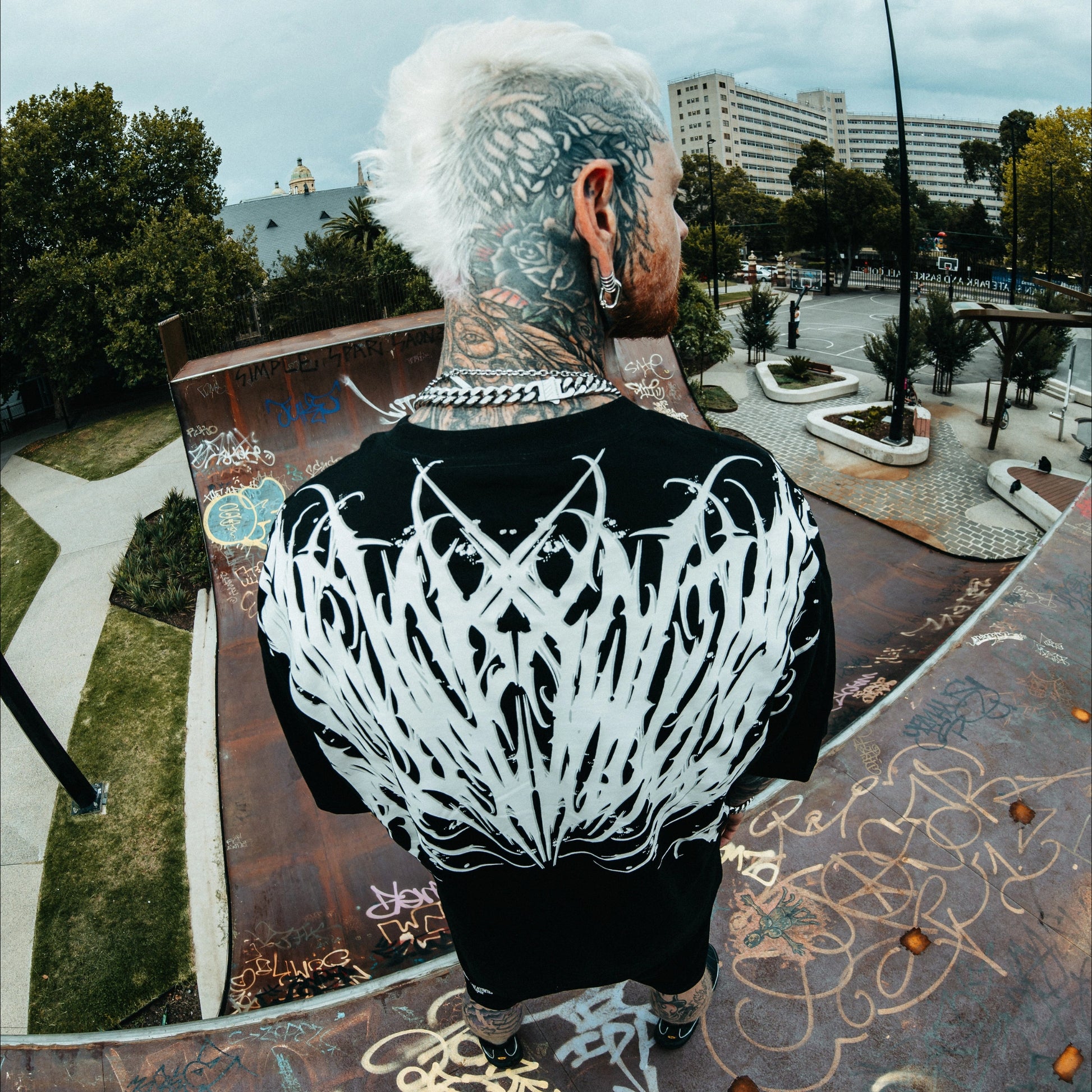 Person with extensive tattoos on a skate park with graffiti and urban elements.