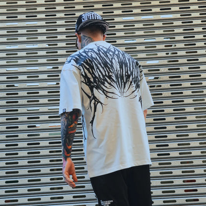 Person wearing a white t-shirt with black graphics, standing in front of a metallic shutter.