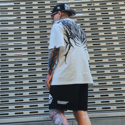 Person wearing a white t-shirt with black graphics and black shorts, standing in front of a metal shutter.