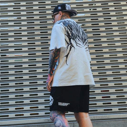 Person wearing a white t-shirt with black graphics and black shorts, standing in front of a metal shutter.
