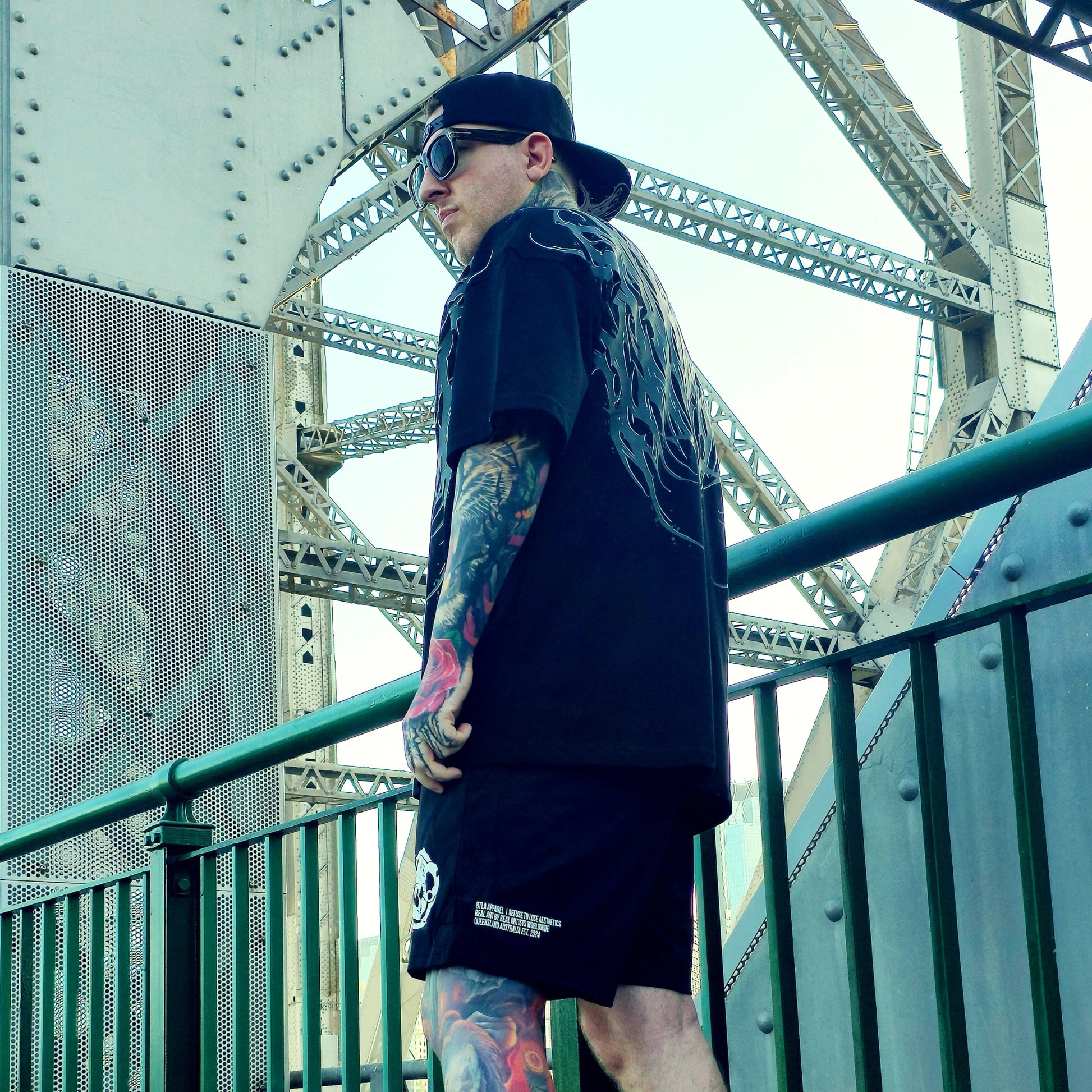 Person wearing a black outfit with tattoos standing on a bridge