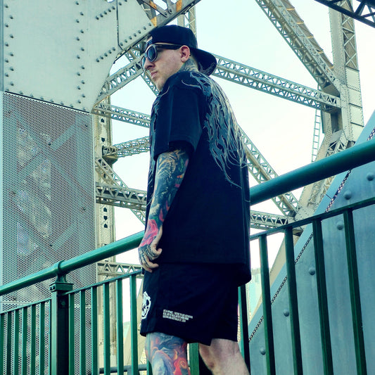 Person wearing a black outfit with tattoos standing on a bridge