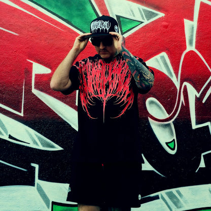 Person wearing a black t-shirt with red graphic design and cap, standing in front of a colorful graffiti wall.