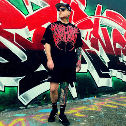 Person wearing a black t-shirt with red design and black shorts standing in front of colorful graffiti.