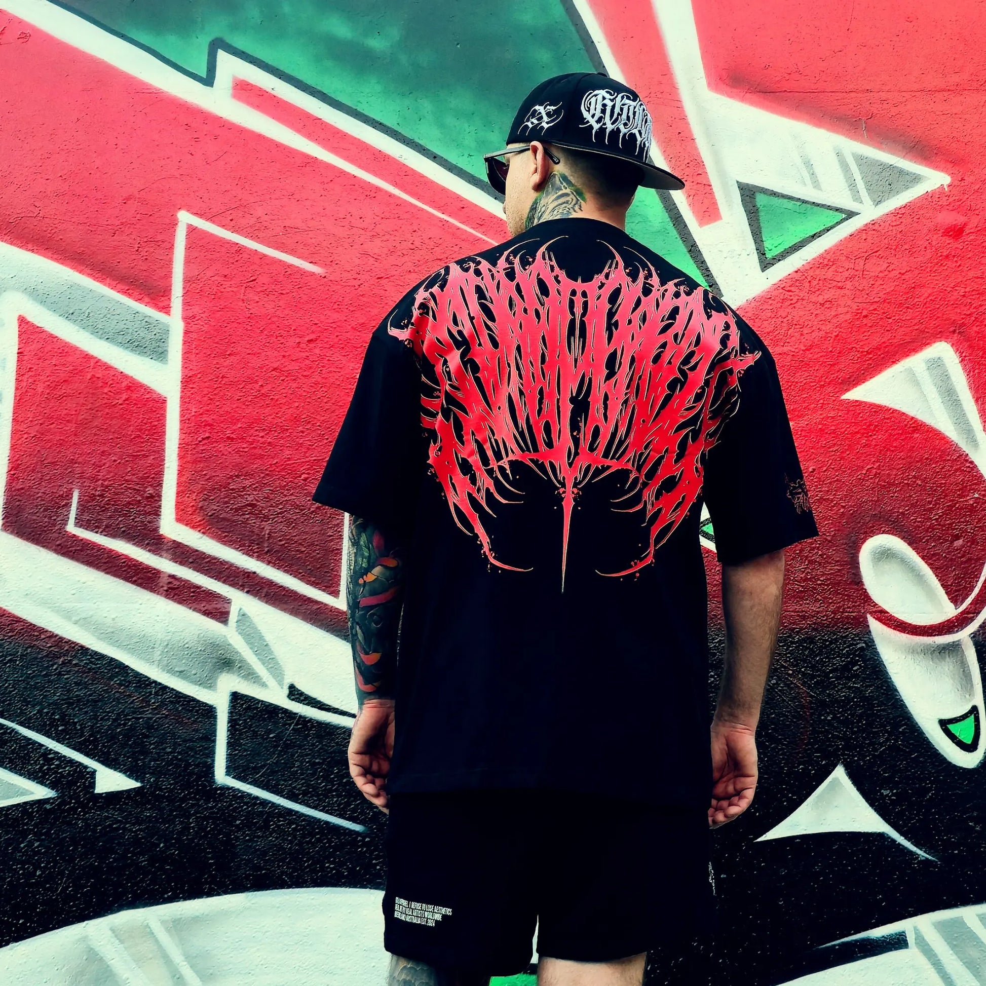 Person wearing a black t-shirt with red and white design, standing in front of a colorful graffiti wall.