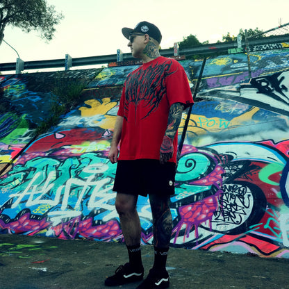 Person wearing a red t-shirt with black graphics in front of a colorful graffiti wall.