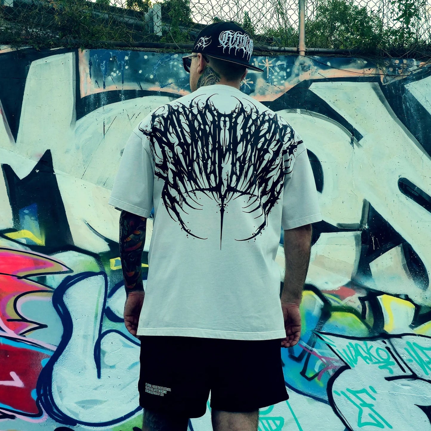 Person wearing a white t-shirt with a black graphic design, standing in front of a colorful graffiti wall.