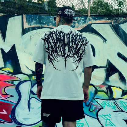 Person wearing a white t-shirt with a black graphic design, standing in front of a colorful graffiti wall.