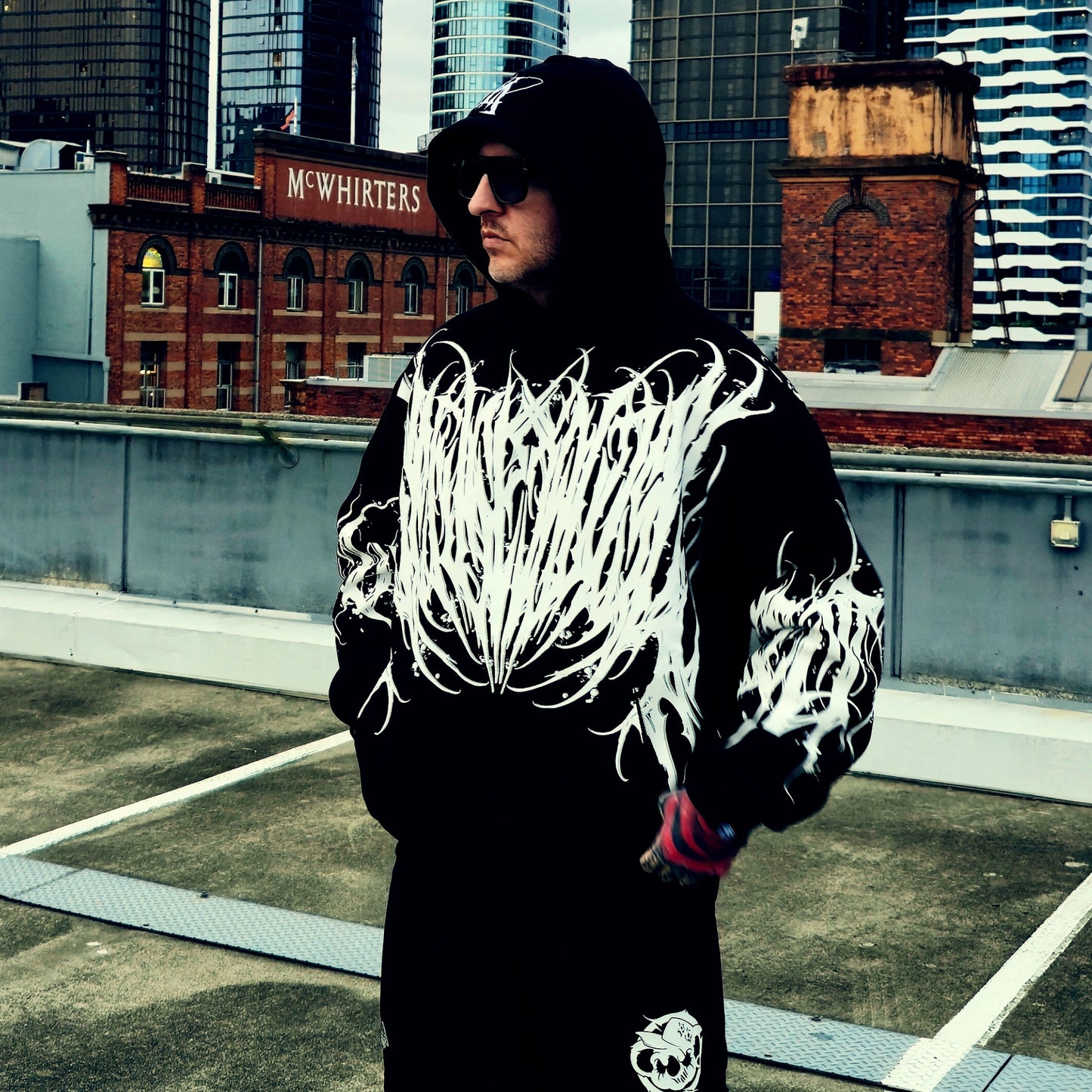 Person wearing a black hoodie with white designs on a rooftop with cityscape background