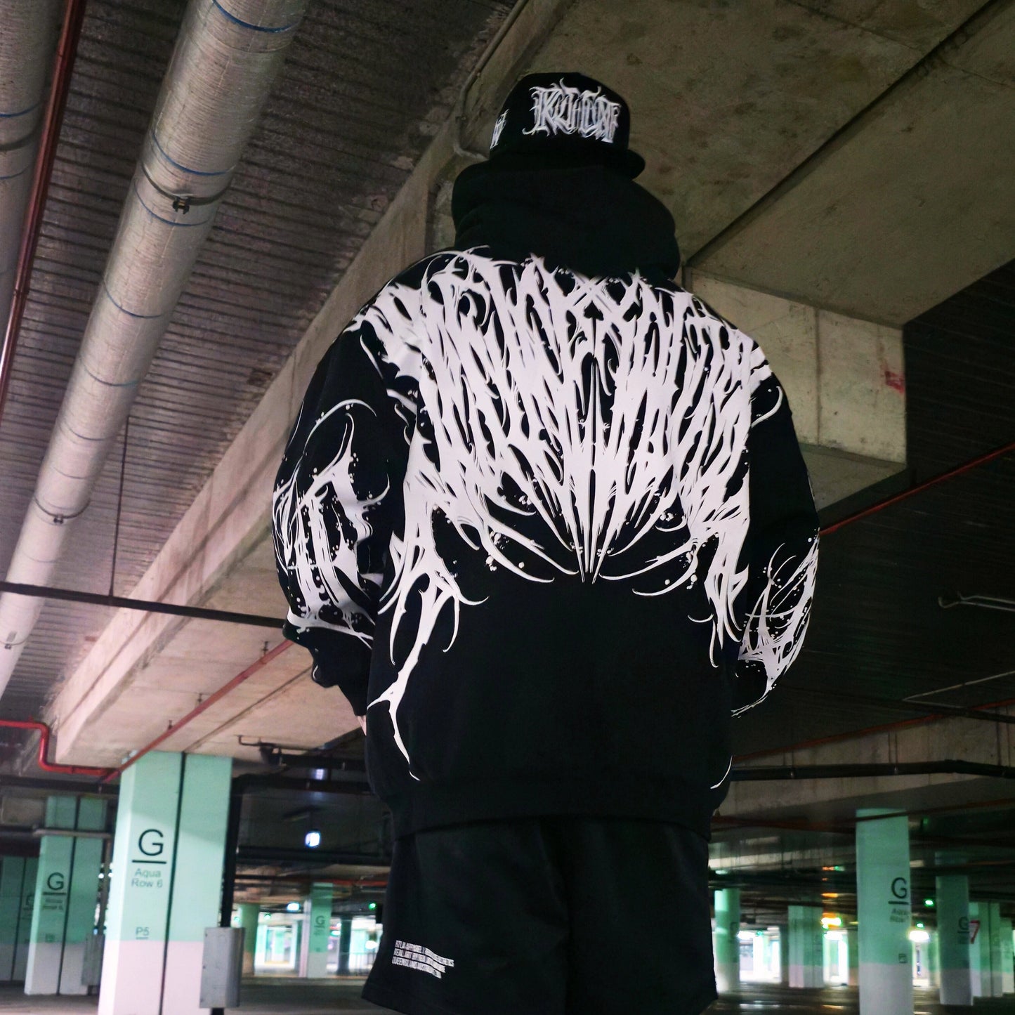 Person wearing a black hoodie with white abstract design in an underground parking garage.