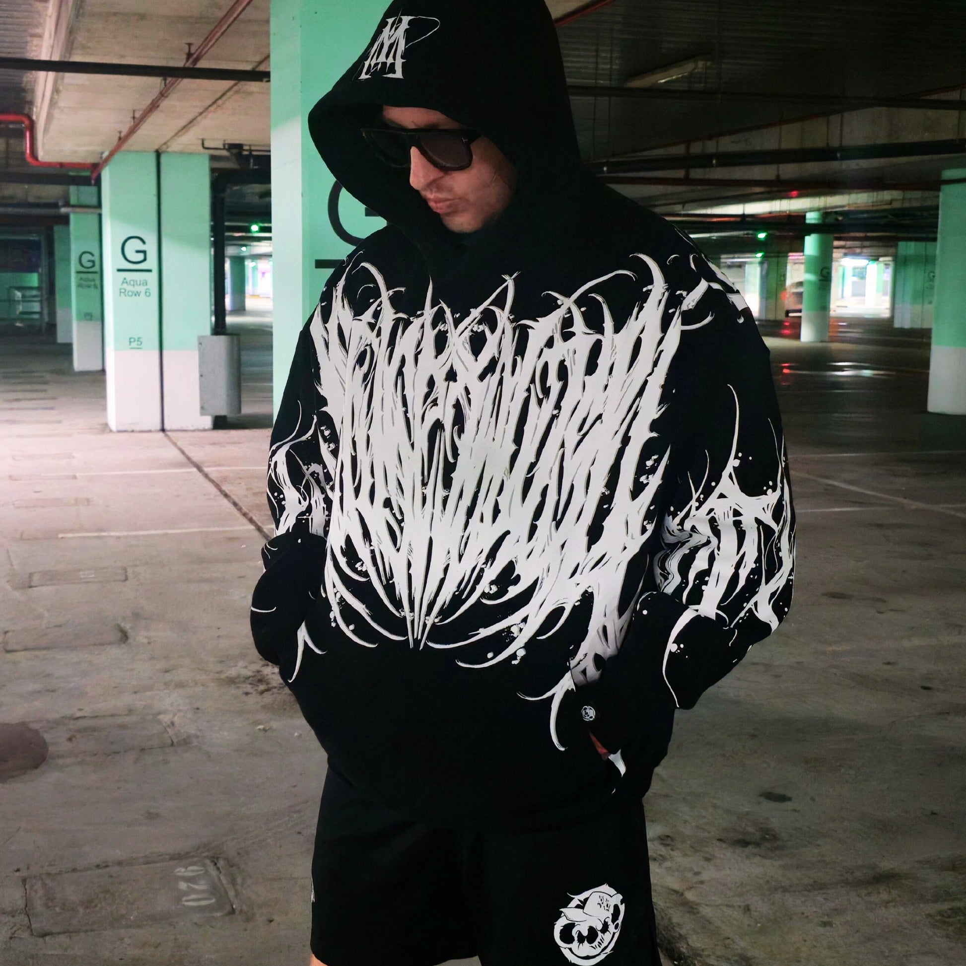 Person wearing a black hoodie with white graphic design in an underground parking garage.