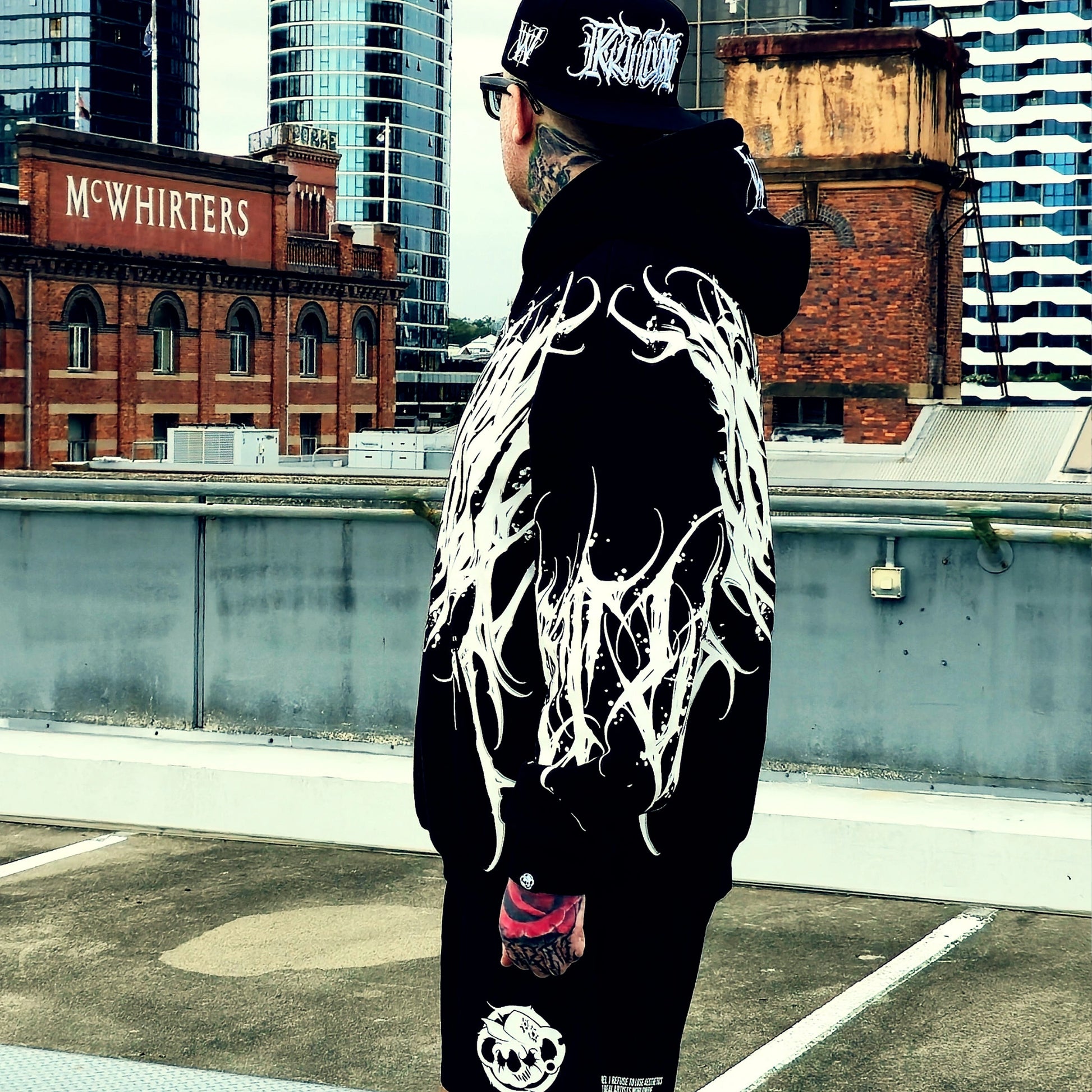 Person wearing a black hoodie with white designs on a rooftop with urban buildings in the background