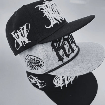 Two snapback caps with embroidered text designs, one primarily black and the other primarily grey, both with 'TRIPLE CROWN' written on them. RTLA-Apparel