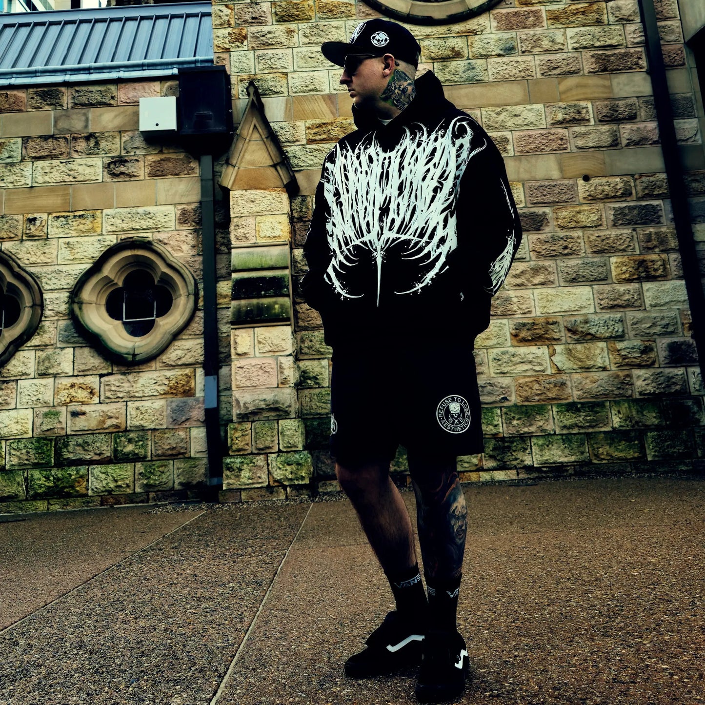 Person wearing a black hoodie with white design in front of a brick wall.