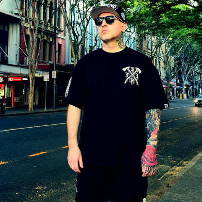 Man wearing a black t-shirt with a logo and sunglasses on a city street.