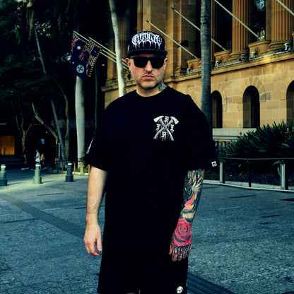 Man wearing a black t-shirt with a logo and a cap, standing in an urban setting.