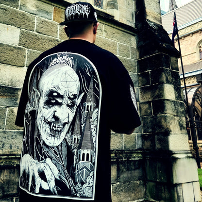 Person wearing a black t-shirt with a graphic design of a skeleton and castle, standing in front of a stone building. RTLA-Apparel
