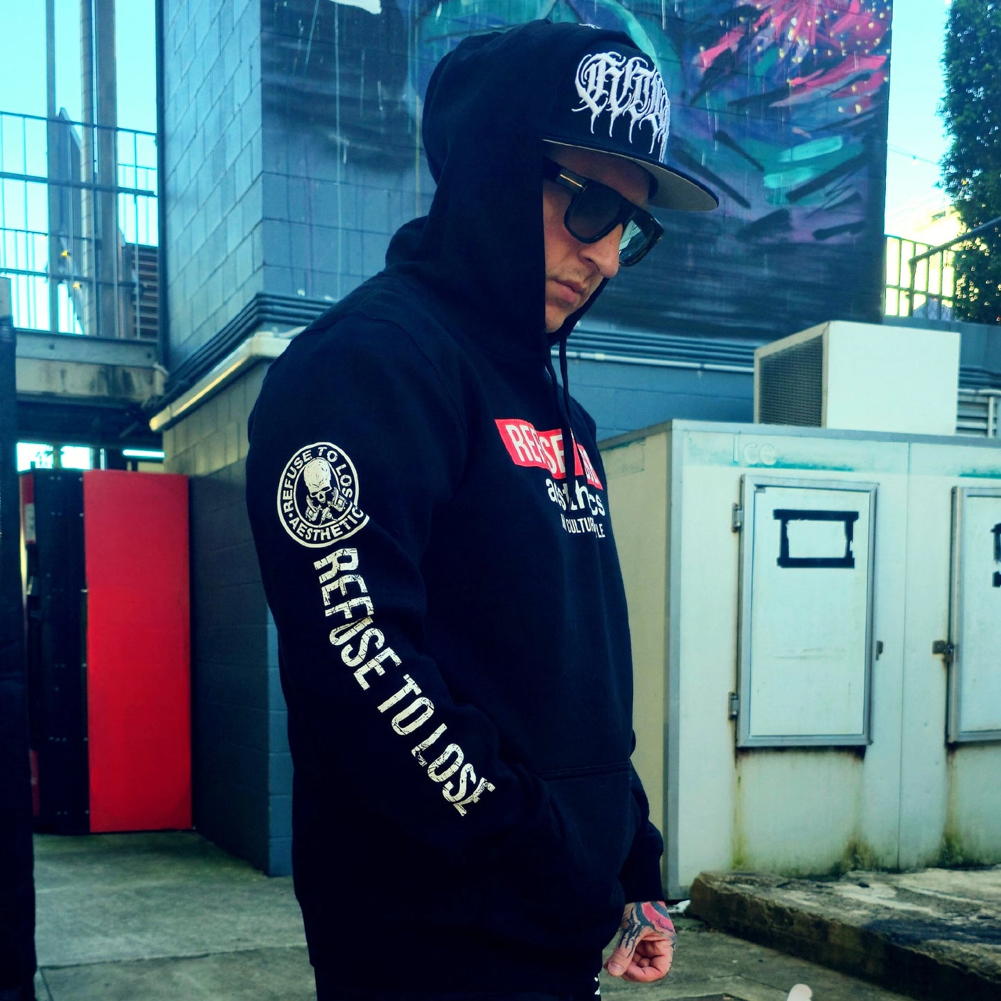 Person wearing a black hoodie with visible branding and text, standing outdoors.