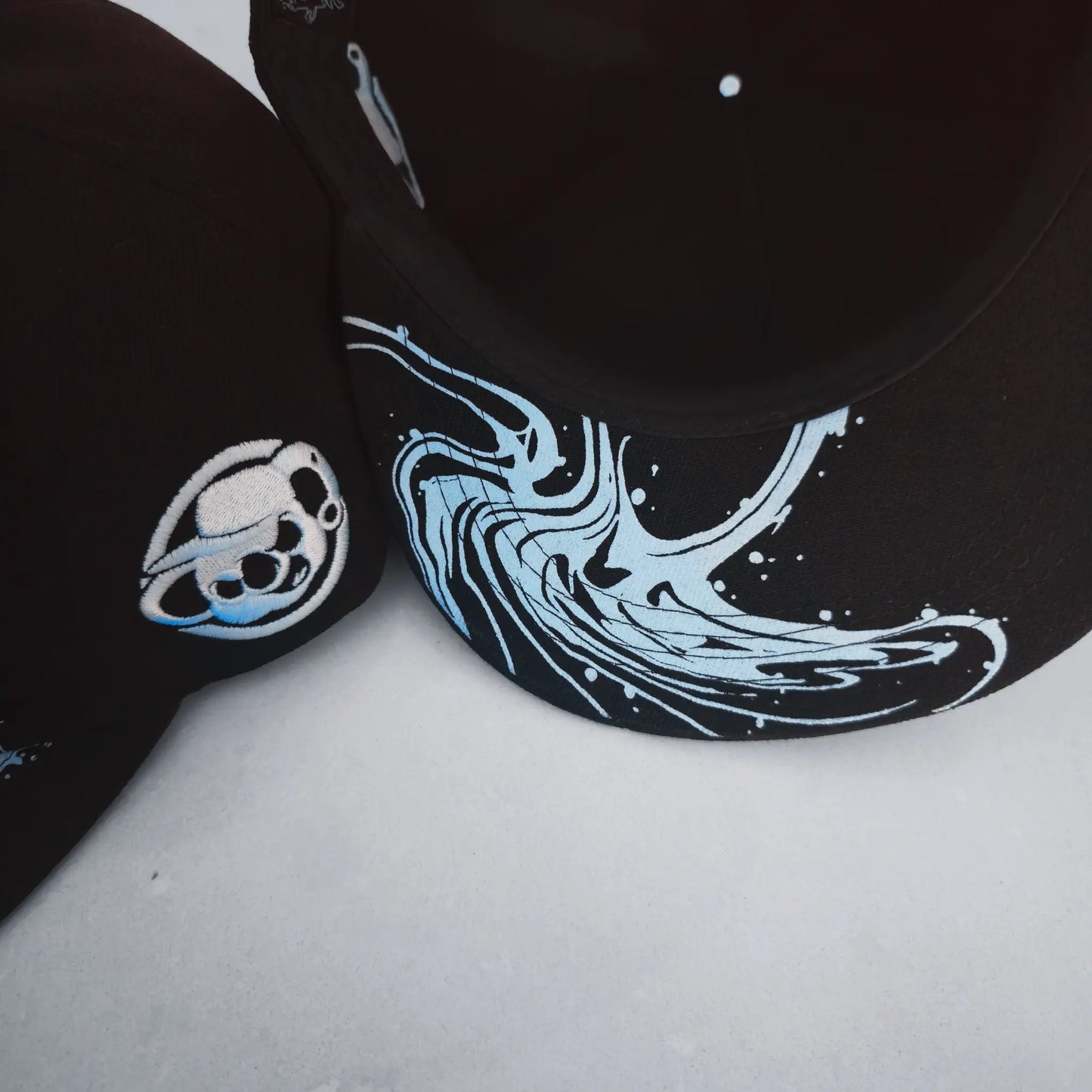 Black cap with blue and white wave design on a light gray background