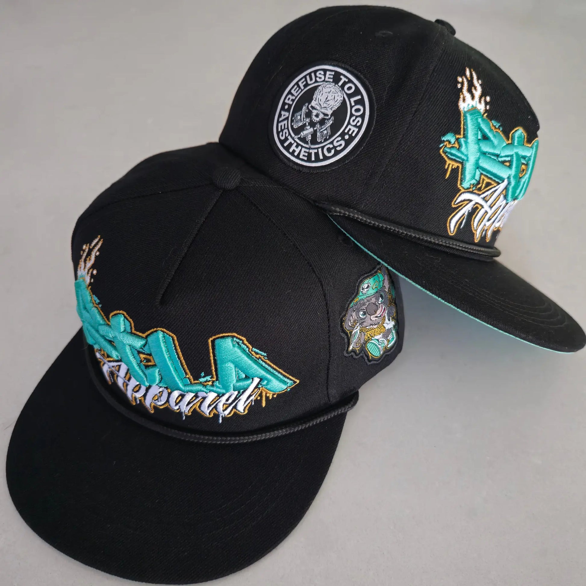 Two black snapback caps with colourful embroidery and under brims, one featuring a snail and the other with abstract designs. RTLA Apparel