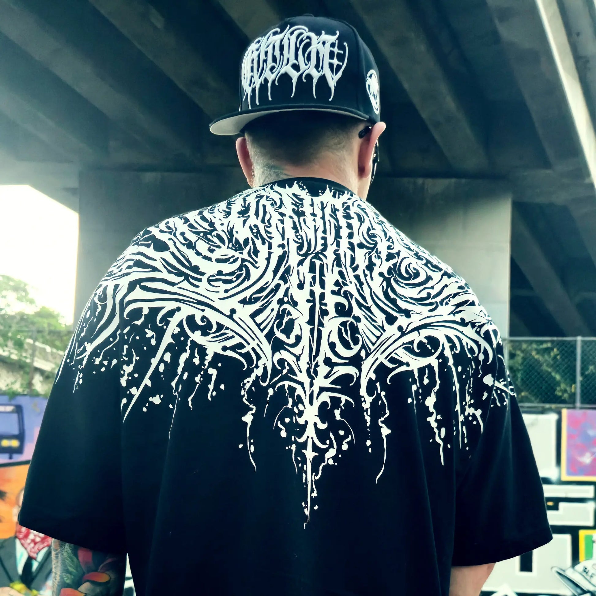Person wearing a black t-shirt with white tribal design and a cap with white logo. RTLA Apparel