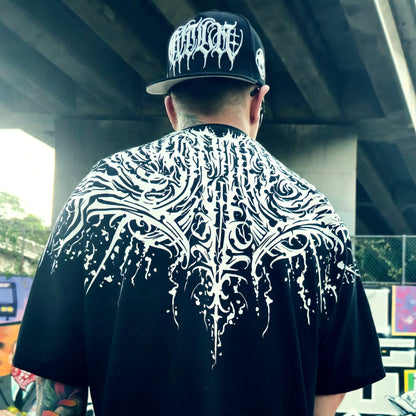 Person wearing a black t-shirt with white tribal design and a cap with white logo. RTLA Apparel