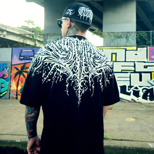 Person wearing a black t-shirt with white intricate design, standing in an urban setting with graffiti. RTLA Apparel