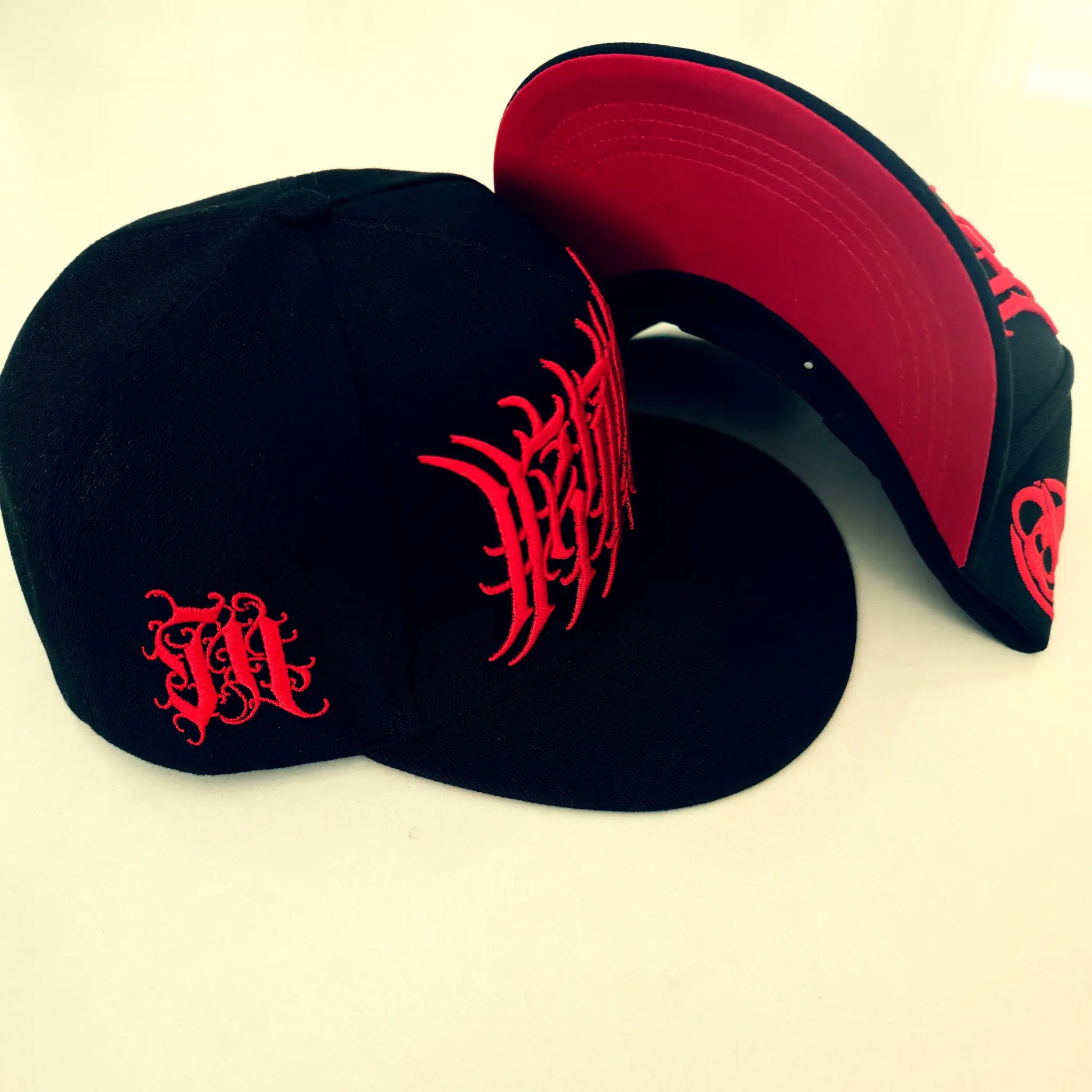 Two black caps with red designs on a beige background