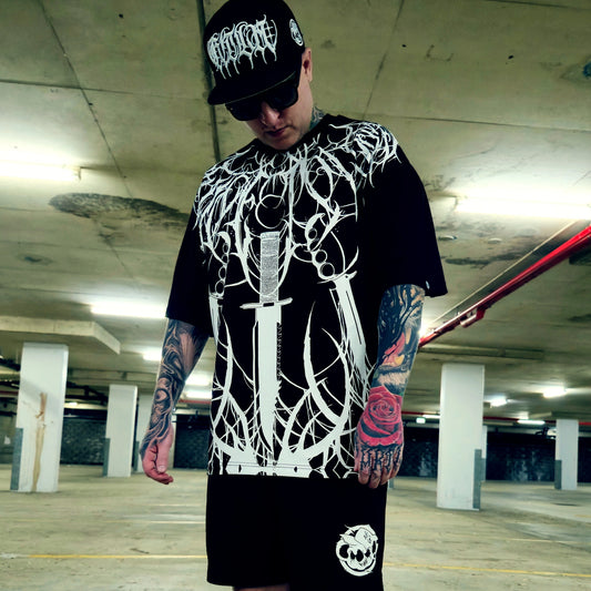 Person wearing a black t-shirt with white graphic design and a black cap in an underground parking lot.