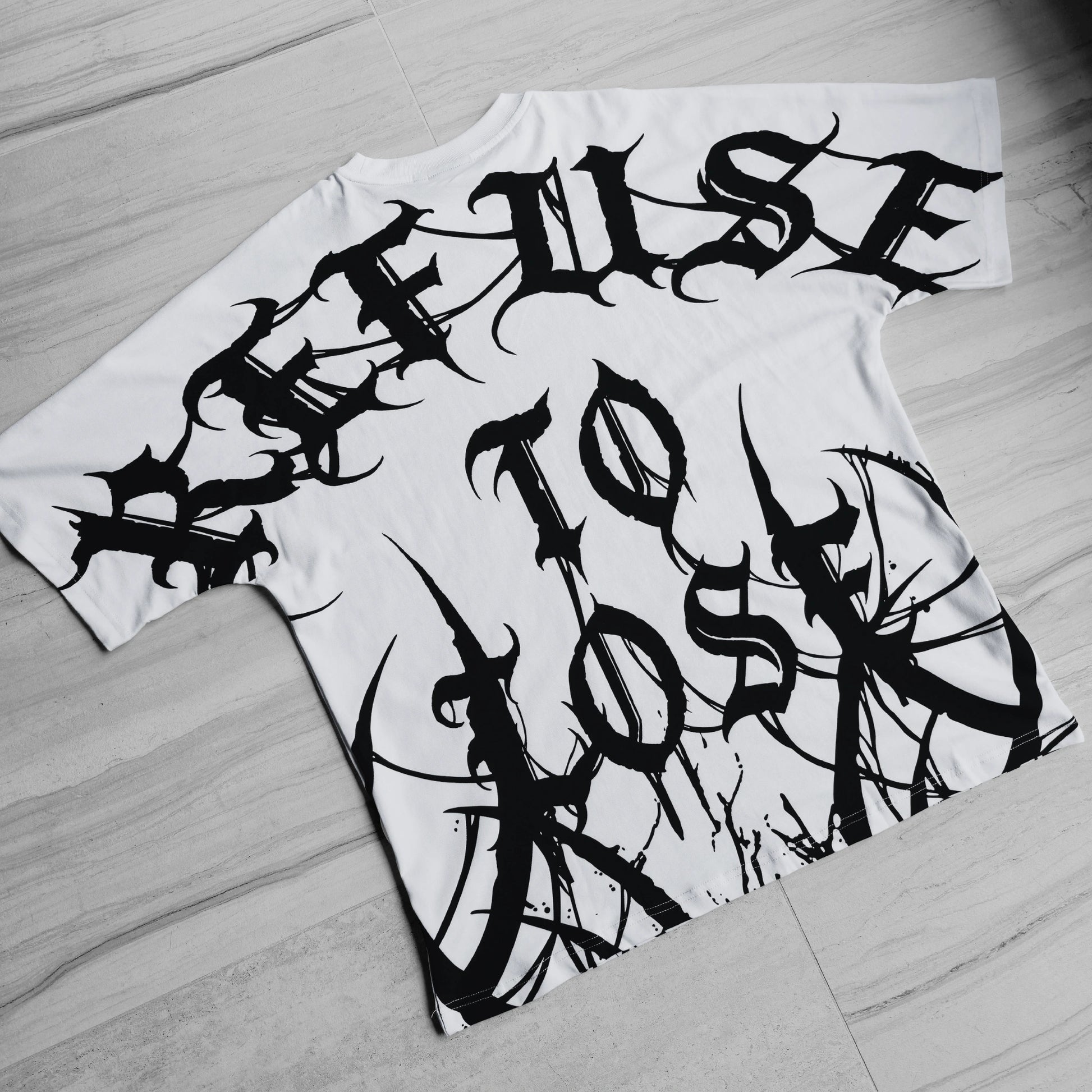 White t-shirt with black graphic text design on a wooden floor.