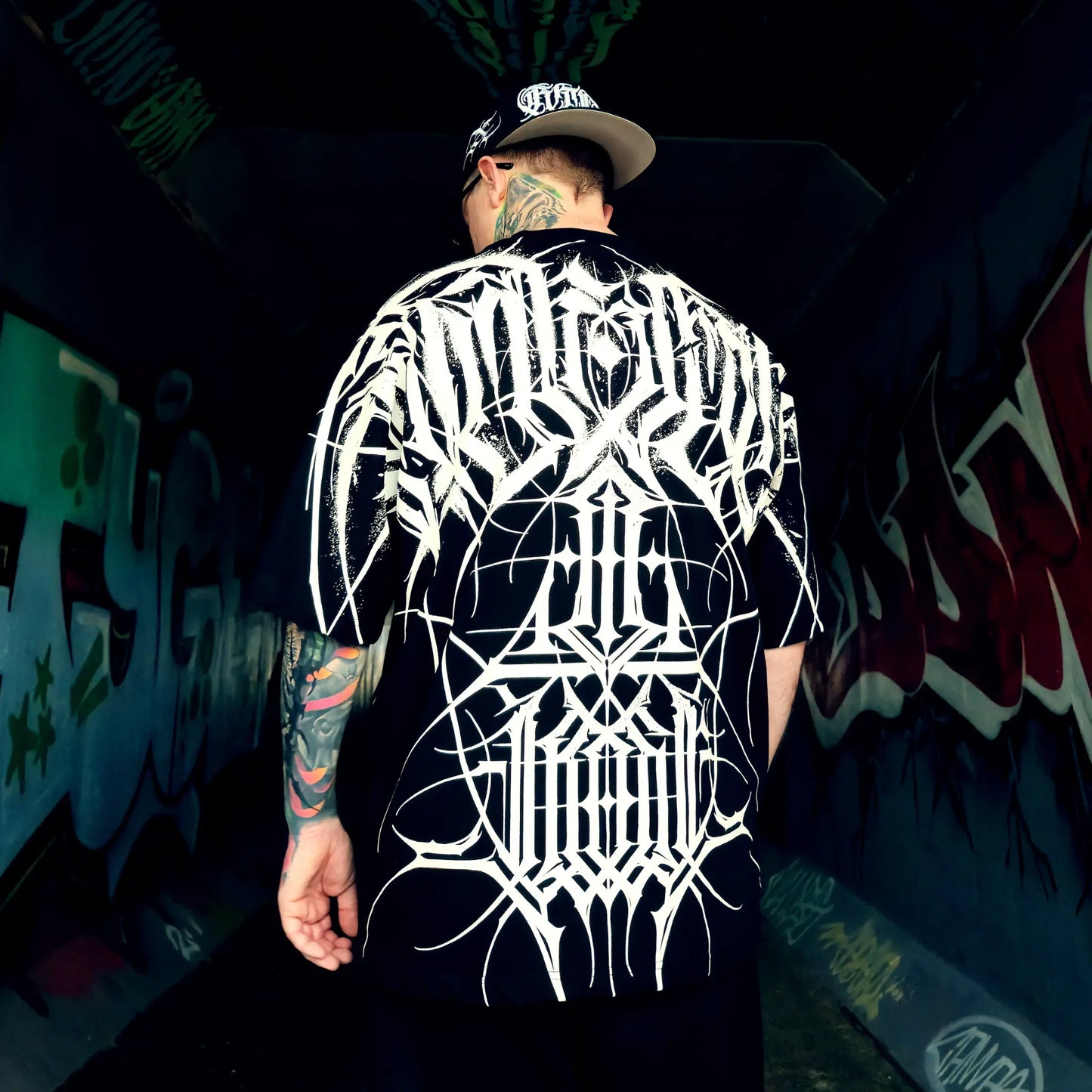 Person wearing a black t-shirt with white graphic design in a graffiti-covered alley.