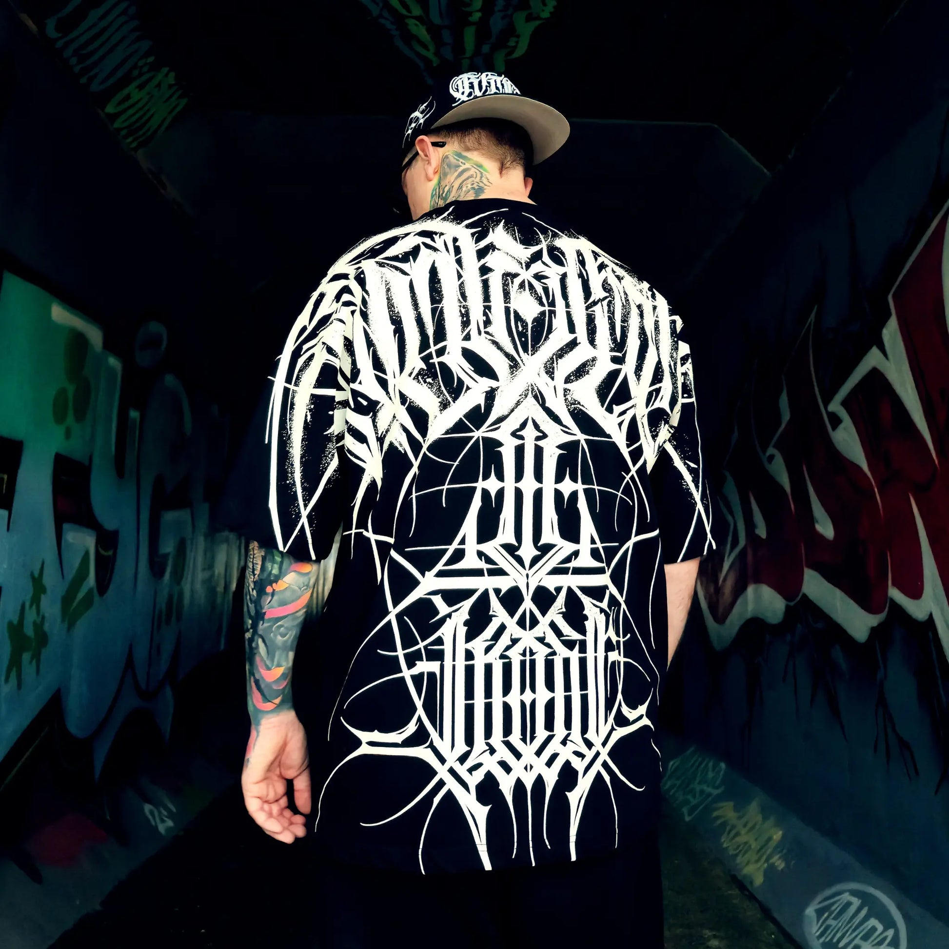 Person wearing a black t-shirt with white graphic design in a graffiti-covered alley.