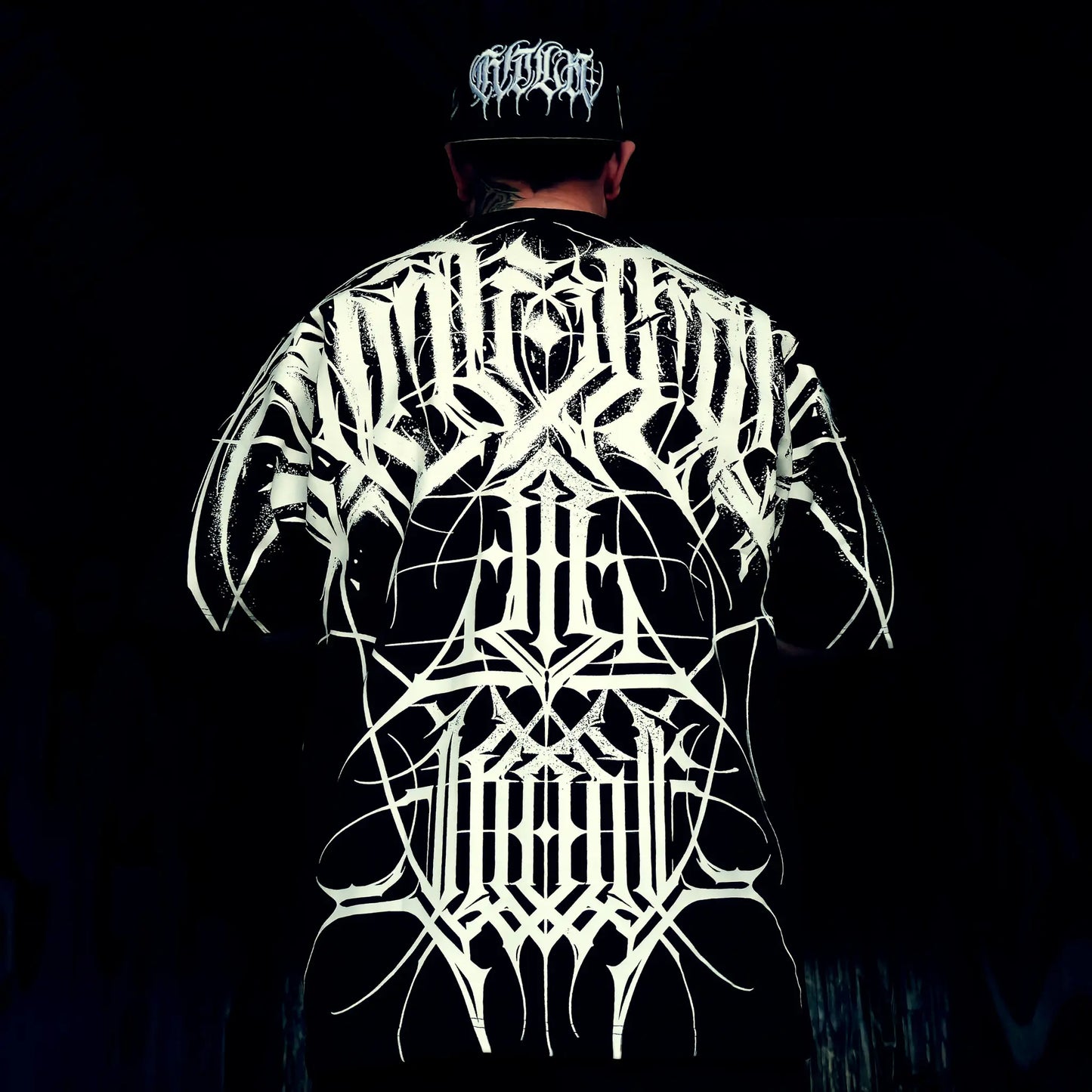 Person wearing a black t-shirt with white intricate designs on the back against a dark background