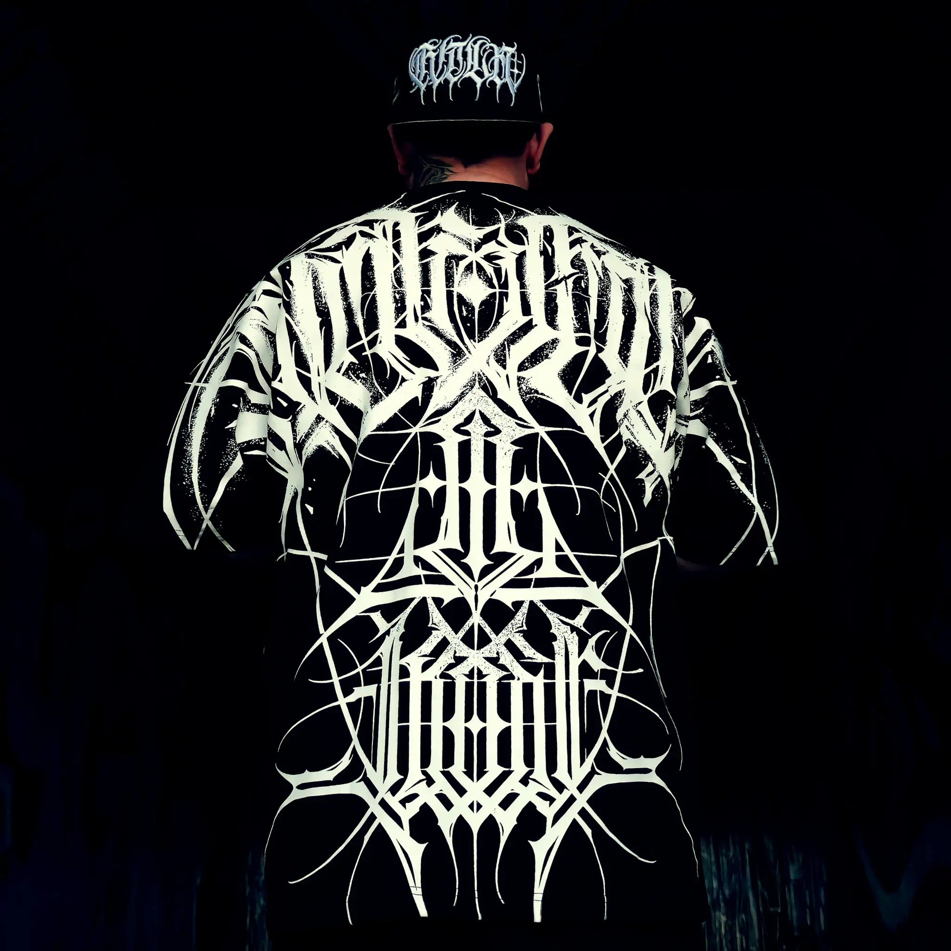 Person wearing a black t-shirt with white intricate designs on the back against a dark background