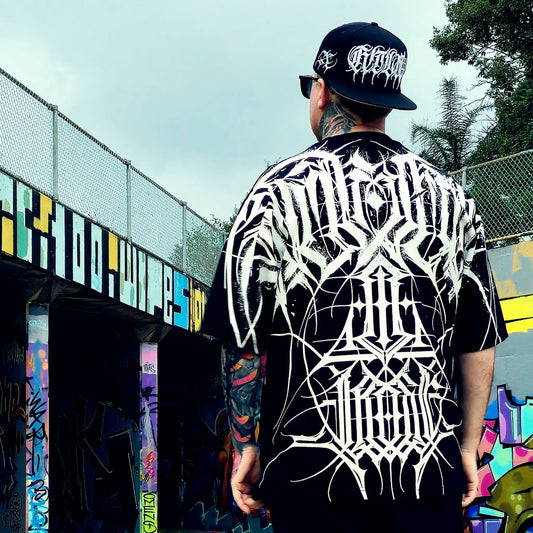 Person wearing a black and white patterned shirt with a cap, standing in front of a colorful mural.