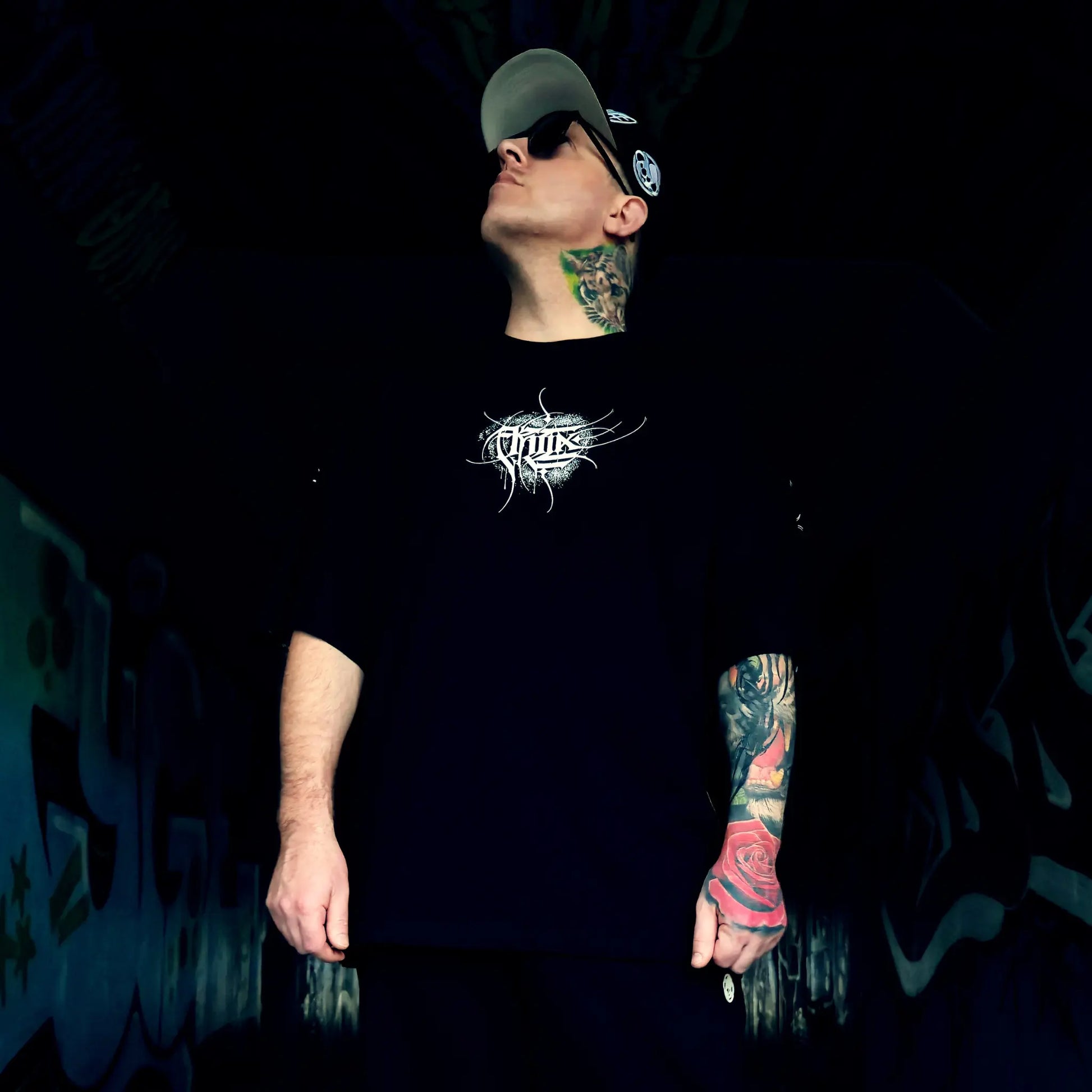 Person wearing a black t-shirt with a logo, standing against a dark background.