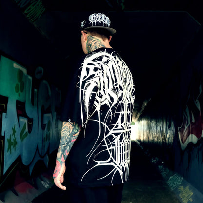 Person wearing a black t-shirt with white graphic design and cap, standing in a graffiti-covered tunnel.