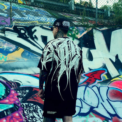 Person wearing a black and white outfit with a cap, standing in front of a colorful graffiti wall.