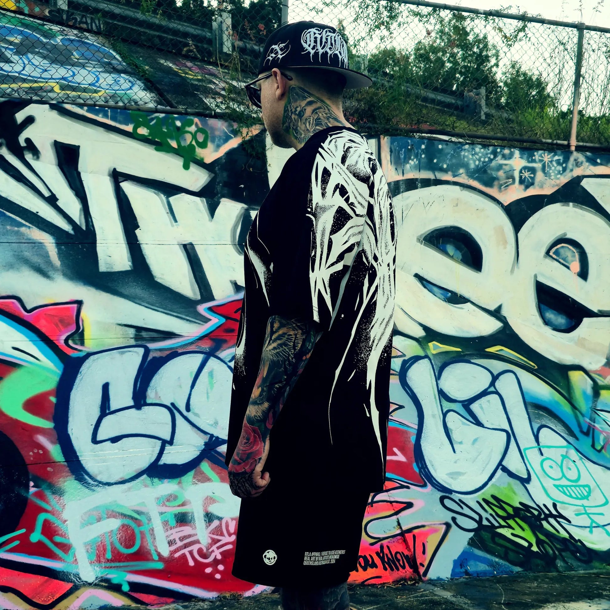 Person wearing a black jacket with white designs in front of a colorful graffiti wall.