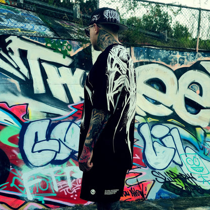 Person wearing a black jacket with white designs in front of a colorful graffiti wall.