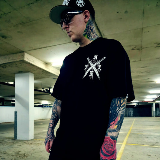 Man wearing a black t-shirt with a logo and a cap in an underground parking lot.