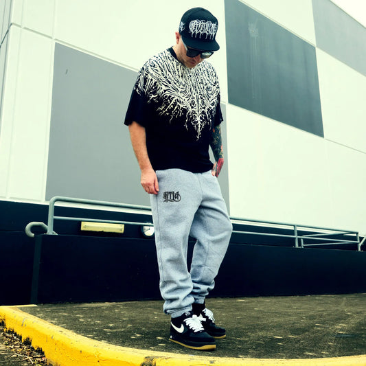 Person wearing a black t-shirt with white graphics, gray sweatpants, and black sneakers in an urban setting.