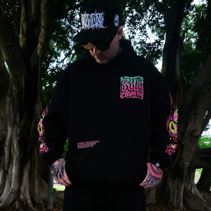 Person wearing a black hoodie with colorful graphics and text, standing in a forest setting.
