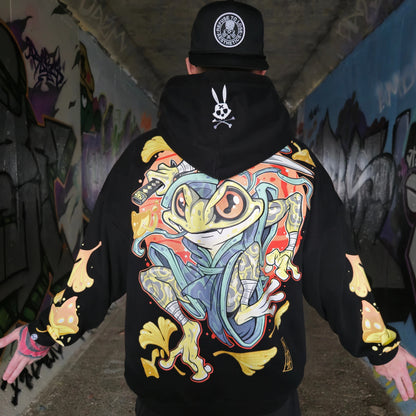 A person wearing a black oversized hoodie with a colourful character design on the back, standing in a graffiti-covered hallway. RTLA Apparel