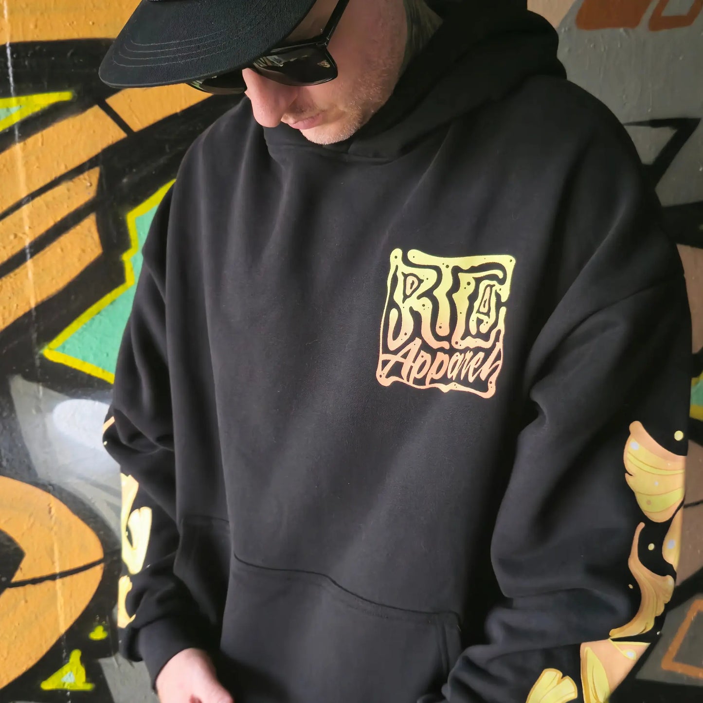 A person wearing a black hoodie with a vibrant multicoloured character RTLA Apparel design.