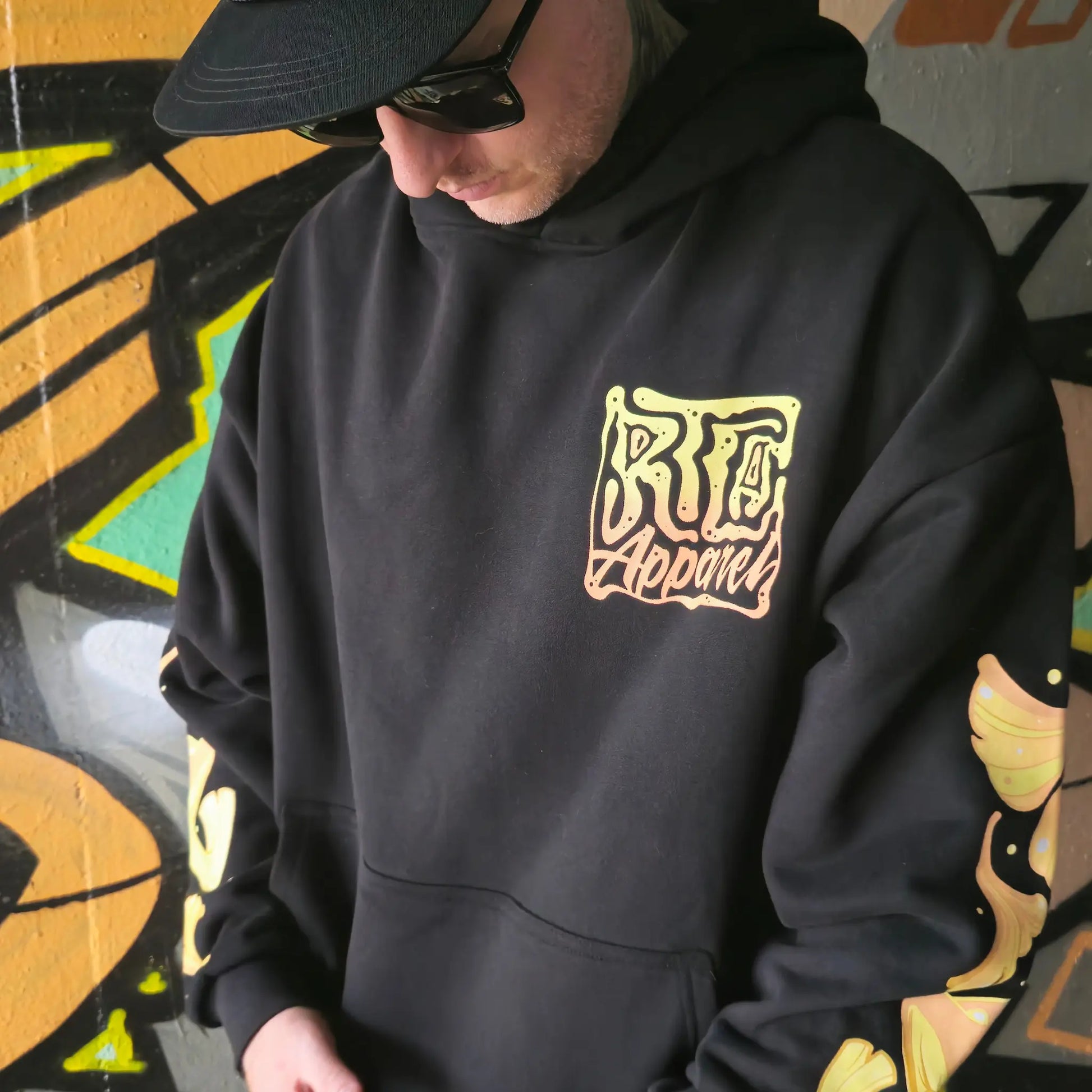 A person wearing a black hoodie with a vibrant multicoloured character RTLA Apparel design.