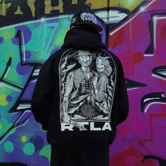 Person wearing a black hoodie with a graphic design in front of a colourful graffiti wall. RTLA-Apparel