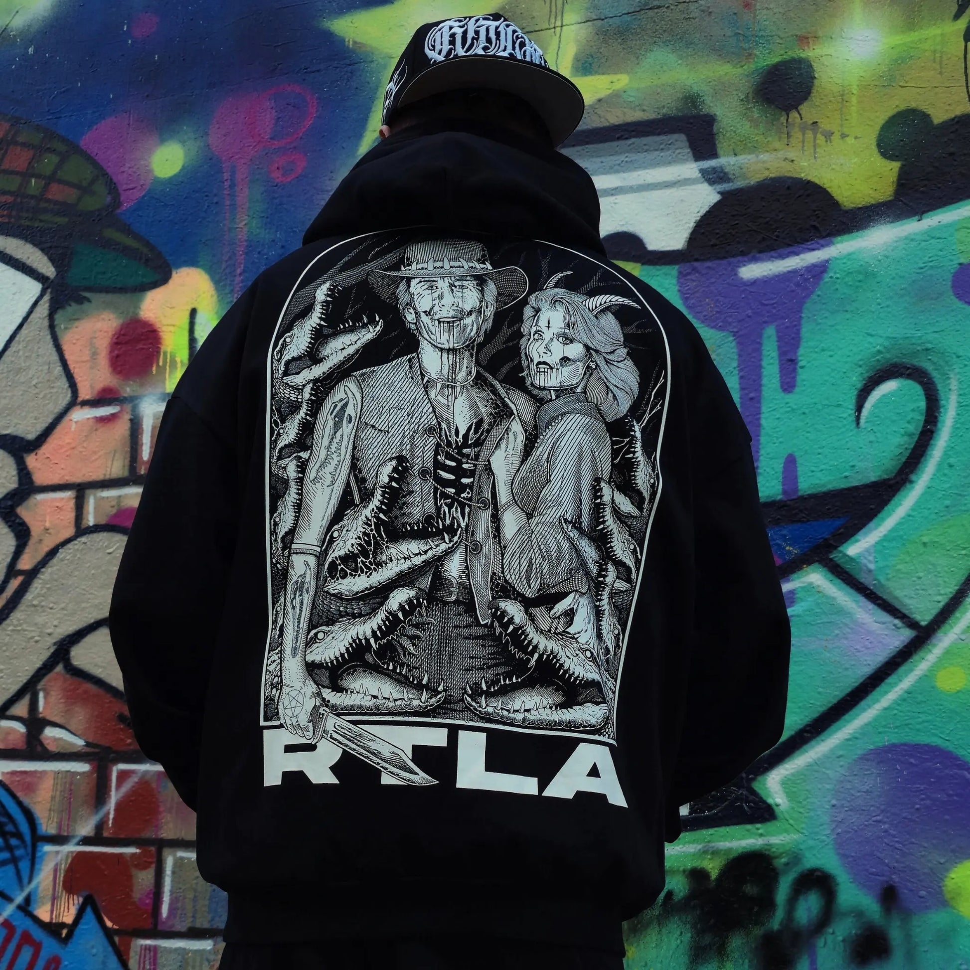Person wearing a black hoodie with a graphic design on the back against a colourful graffiti background. RTLA-Apparel