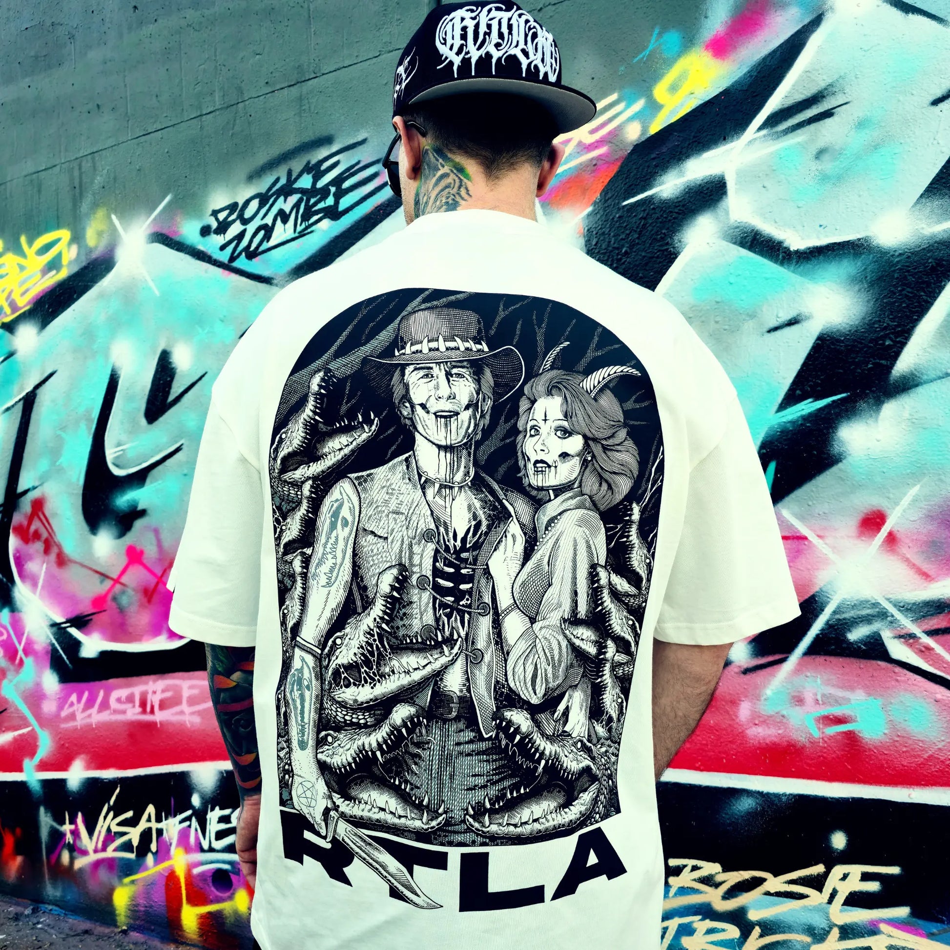 Person wearing a white t-shirt with a black and white graphic design, standing in front of a colourful graffiti wall. RTLA-Apparel