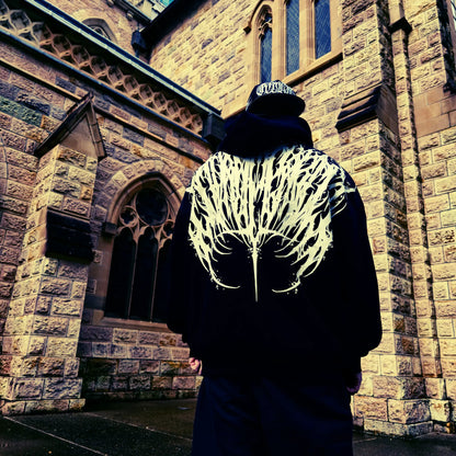 Person wearing a dark hoodie with a white pattern in front of a stone building